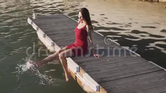 穿着衣服的女人坐在木墩上双脚在水里摆动动作缓慢视频的预览图