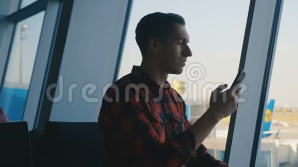 年轻男性旅客在机场候机楼使用智能手机视频的预览图