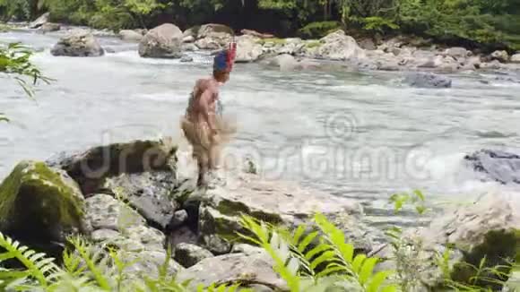 土著男子在河流边缘的岩石上跳跃视频的预览图