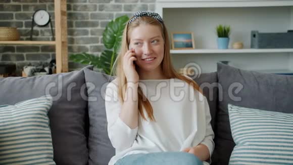 在现代公寓里坐在沙发上笑着玩手机的快乐女孩视频的预览图