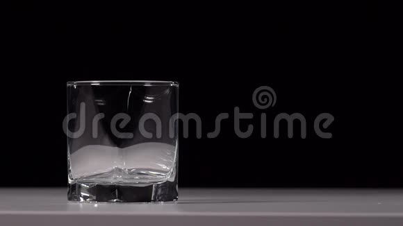在黑色背景的白色桌子上将水倒入透明玻璃的工作室镜头视频的预览图