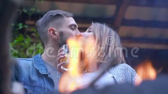 年轻的白种人夫妇站在户外烧烤的地方喝着一杯果汁拥抱和亲吻有爱心的人视频的预览图