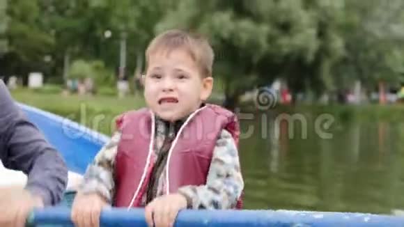 可爱的小男孩穿着救生衣在湖上飞快地排着坐在船上的小可爱孩子的近景有趣的孩子划桨视频的预览图