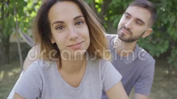 青年男女在夏季花园放松的肖像他摸着妻子的头发她微笑着看着视频的预览图