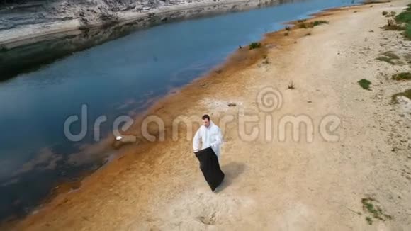 一个穿着防护服的人在干燥和污染的河流岸边收集塑料垃圾的鸟瞰图显示视频的预览图