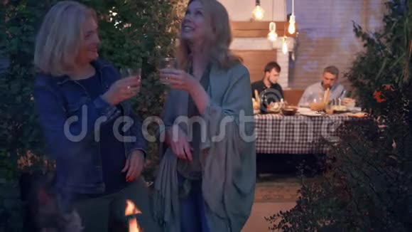 两个成熟的女朋友在前台聊天站在烧烤前喝酒而她们的丈夫则在聊天视频的预览图