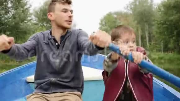 快乐的爸爸和儿子在公园里坐船聊天年轻的父亲和他可爱的小儿子在湖边划船爱情视频的预览图