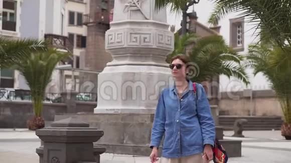 在一个古老的欧洲城市的街道上带着眼镜和牛仔的快乐女游客慢动作女人微笑着视频的预览图