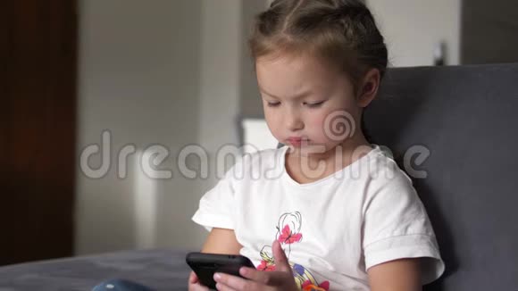 休闲儿童坐在家里的沙发上玩和触摸手机视频的预览图