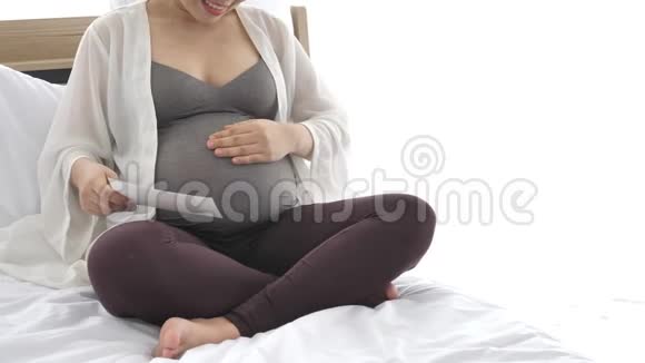 孕妇在卧室的家中在床上用手轻轻触摸腹部同时看乳房X光照片人们的生活方式视频的预览图