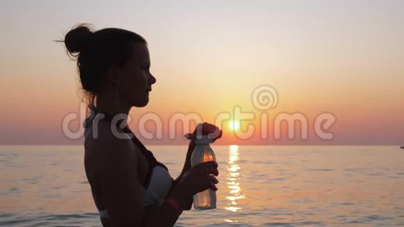 女孩在日落时在海边或海边喝水视频的预览图