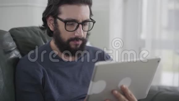 使用平板电脑的眼镜中的浓白种人的肖像年轻留胡子的商人处理有关视频的预览图