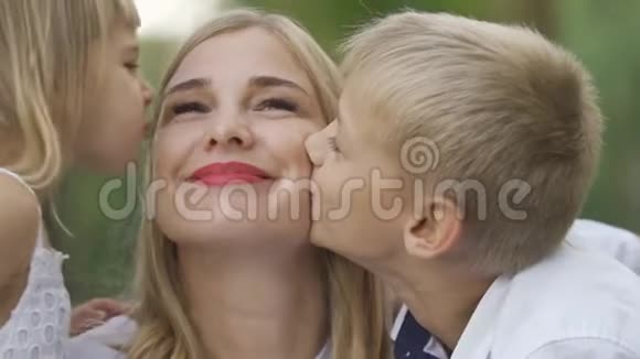 小女孩和男孩亲吻妈妈脸颊的特写公园里的幸福家庭户外休闲母亲父母身份视频的预览图