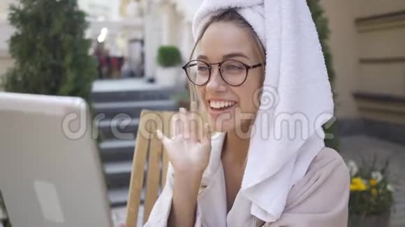 戴眼镜穿浴袍头戴毛巾的年轻女子在平板电脑上用照相机与朋友交谈的肖像视频的预览图