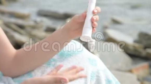 特写的年轻女性双手在海边从一根管子里挤出防晒霜每年夏季护理概念视频的预览图