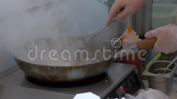厨师在炒锅上做亚洲面条加入酱汁在电炉上用烟搅拌视频的预览图