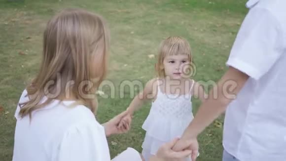 可爱的小女孩牵着父母的手在公园里快乐的孩子和家人在一起童年父母身份视频的预览图