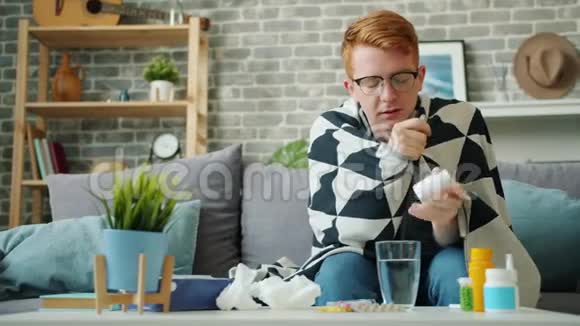 不健康的年轻人吃药喝水坐在沙发上毯子下视频的预览图