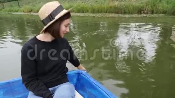 戴草帽的女人把手放在水里快乐的女孩在湖边的船上休息女人对着镜头微笑女孩在水上牵着手掌视频的预览图