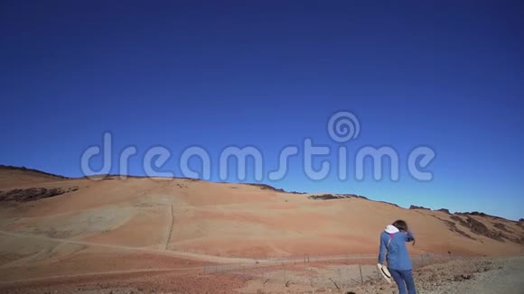一个年轻的女徒步旅行者走过一个沙漠火山景观在山上很高穿牛仔布的女人大角度的视频的预览图