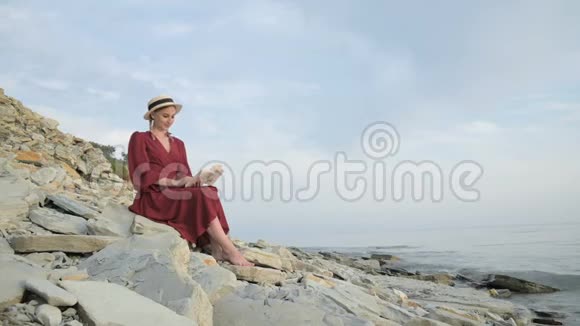 一幅美丽迷人的白种人女孩的肖像她穿着一件夏日红色连衣裙和一顶草帽怀里抱着一本书视频的预览图