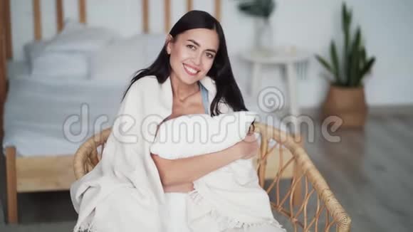 裹着格子的女人坐在扶手椅上抱着枕头微笑着看着镜头视频的预览图
