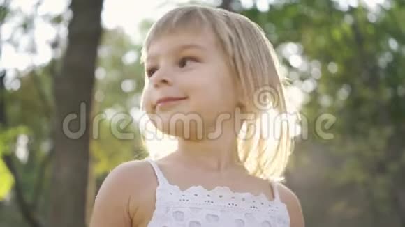 特写一个小可爱的女孩看着相机指着别处阳光下公园里美丽的孩子的肖像视频的预览图