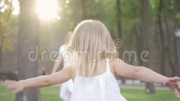 从后面看到可爱的小女孩朝她妈妈跑去女人笑着拥抱女儿公园里的幸福家庭一个视频的预览图