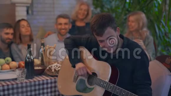 一群人喝着酒微笑着坐在桌子的背景上年轻人在弹吉他视频的预览图
