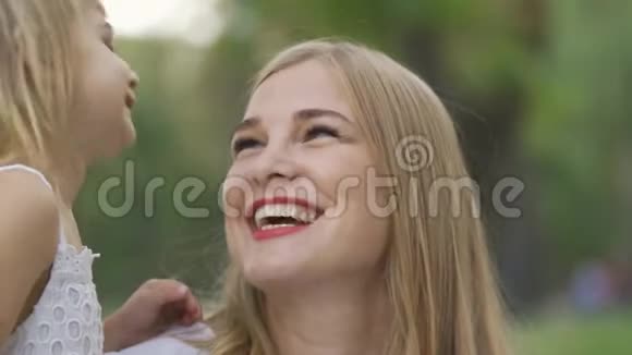 可爱的小女孩舔着妈妈的脸颊有两个孩子的女人花时间在户外公园里的幸福家庭视频的预览图