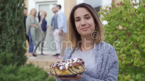 快乐的白种人女人带着蛋糕微笑着看着站在前台的镜头和人在一起交谈视频的预览图