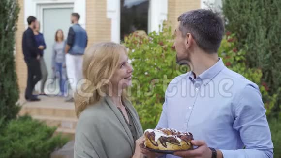 幸福的成熟夫妇带着蛋糕微笑着看着站在前台的镜头和人在一起交谈视频的预览图