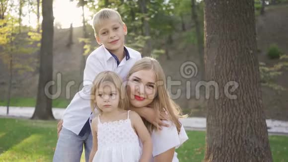 漂亮的女人带着两个孩子看着摄像机微笑一个小可爱的女孩指着别处幸福家庭视频的预览图