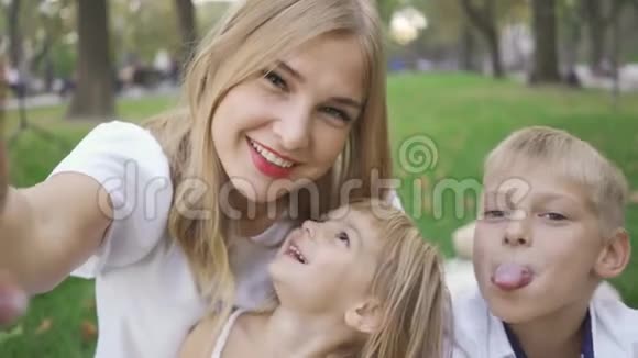 漂亮的高加索女人和她的两个孩子看着镜头微笑女人和孩子自拍小男孩女孩视频的预览图