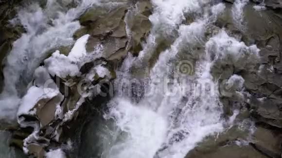在冬天从山溪和石头急流中迅速流出的水和雪瀑布视频的预览图