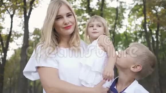年轻的金发女人抱着小女儿而大儿子站在他们旁边有两个孩子的幸福家庭视频的预览图