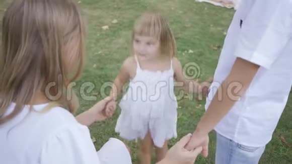 快乐的小女孩在公园里牵着父母的手跳起来孩子和家人在一起童年视频的预览图