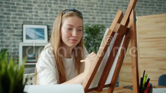 幸福的年轻女士坐在画架上用彩色铅笔在家画画画视频的预览图