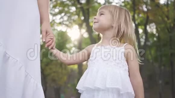 一个穿着白色裙子的小女孩站在公园或森林里牵着成年女人的手微笑着儿童保育视频的预览图