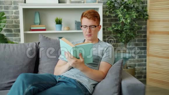 戴眼镜看书坐在公寓沙发上微笑的帅哥视频的预览图