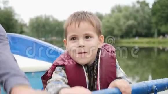 小可爱的孩子在城市公园的湖边划船可爱的男孩对着湖边的摄像机微笑小男孩想划船视频的预览图