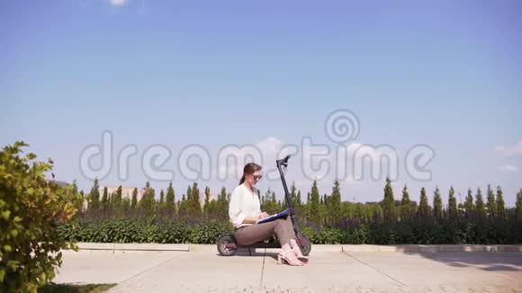 城市景观中的现代上班族迷人的苗条女孩坐在公园里的电动踏板车上视频的预览图