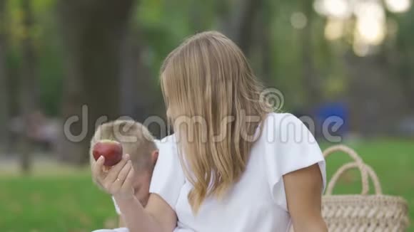可爱的白种人女人和小男孩坐在草地上手里拿着苹果母子花时间视频的预览图