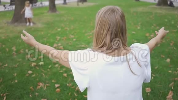 后景的年轻白种人妇女坐在公园里等待她的女儿拥抱可爱的小女孩在奔跑视频的预览图