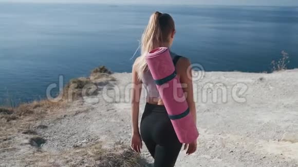 背面穿着运动服的女孩带着体操垫来到山顶视频的预览图