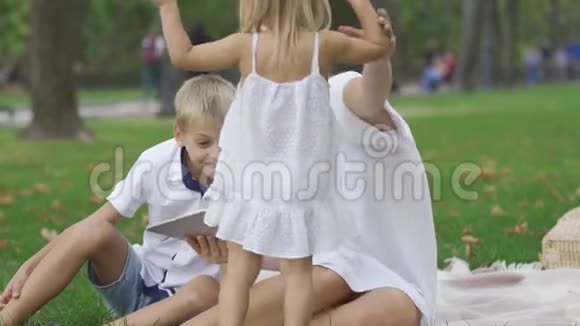可爱的白种人女人和两个孩子花时间在户外那个女人在平板电脑上给她的孩子看东西视频的预览图