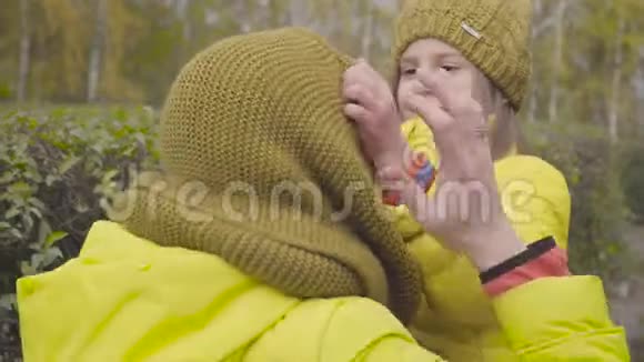 微笑白种人女孩把芥末围巾固定在母亲头上女儿穿着类似的黄色外套的女人视频的预览图