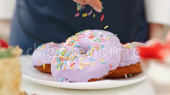糖果师把五颜六色的糖果巧克力洒在磨砂的甜甜圈上近距离拍摄4k红色相机视频的预览图