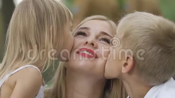 后视可爱的小女孩和男孩亲吻母亲的脸颊女人笑着拥抱儿子和女儿幸福家庭视频的预览图
