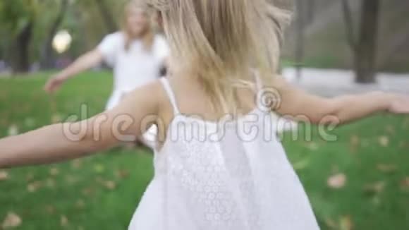在阳光下小金发女孩朝她母亲跑去漂亮的年轻女子坐在草地上视频的预览图